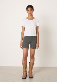 Weißes Baumwoll-T-Shirt mit kurzen Ärmeln, kombiniert mit grauen, eng anliegenden Shorts und braunen kniehohen Stiefeln mit schwarzen Sohlen und Schnallenakzenten.