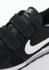 Czarny sneaker z zapięciem na rzep, wykonany z zamszu i siateczki. Biały swoosh Nike i logo na czarnym tle. Gumowa podeszwa.