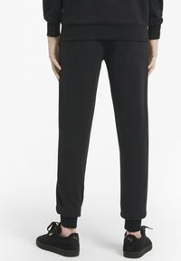 Svarta träningsoveraller med elastiska muddar och midja, tillverkade av mjukt tyg. Kombineras med svarta sneakers med guldaccenter.