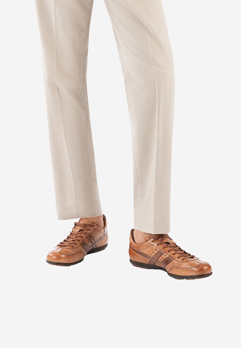 Baskets en cuir brun avec une texture lisse, présentant des accents foncés, une pointe ronde et un laçage, associées à un pantalon beige clair.