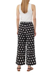 Pantalon à jambes larges en tissu noir avec de grands pois blancs, doté d'une taille élastique et d'un ajustement confortable. Associé à un débardeur blanc.