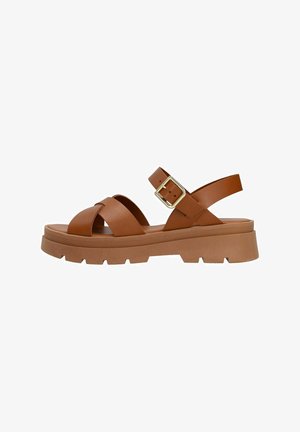Sandales en cuir marron avec un design de lanières entrecroisées, une sangle de cheville réglable et une semelle en caoutchouc épaisse présentant une texture striée et une hauteur modérée.
