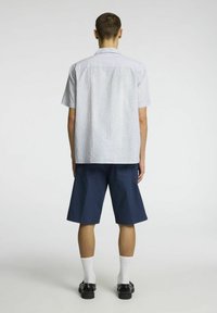 Košile s krátkým rukávem světle modré pruhy v kombinaci s námořnickými šortkami. Oblečení má uvolněný střih, boční kapsy a bílé ponožky s černými botami.