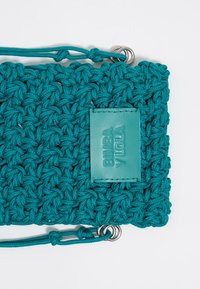 Borsa all'uncinetto color acquamarina con finitura testurizzata, etichetta in pelle con il nome del marchio impresso e strap regolabili con anelli in metallo.