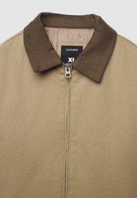 Beżowa kurtka z brązowym kołnierzem, zamek błyskawiczny z przodu i widoczną metką Terranova XL wewnątrz kołnierza.