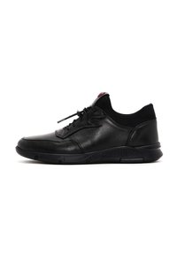 Zapatilla de cuero negra con cuello de malla texturada en negro, punta redonda y suela de goma. Presenta un sistema de cordones tradicional y un sutil acento rojo.