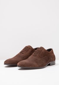 Chaussures oxford en daim marron avec un bout pointu, un design de laçage à cinq œillets, une texture lisse et un petit talon empilé.