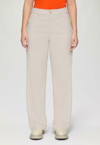 Beige wijde broek van lichtgewicht stof, met een sluiting aan de voorkant met knoop en zijzakken, aangevuld met crèmekleurig schoeisel.