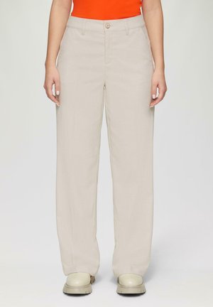Pantalons beige à jambes larges en tissu léger, avec une fermeture à bouton à l'avant et des poches latérales, accompagnés de chaussures de couleur crème.