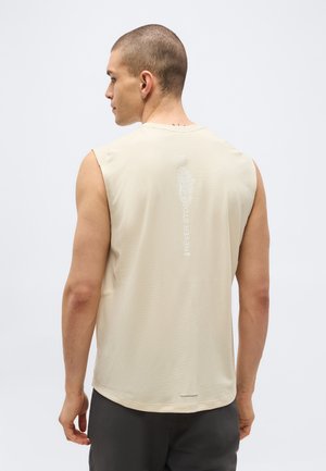 Homme aux cheveux courts portant un débardeur beige avec un logo discret "Never Stop" dans le dos, tourné dos à la caméra.