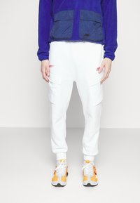 Nike blå fleecejacka med två frontfickor, parat med vita sweatpants med cargofickor och röda randdetaljer, bärs med färgglada sneakers.