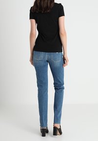 Mustapaitainen lyhythihainen paita, joka on yhdistetty sinisiin suoriin farkkuihin ja mustiin korkokenkiin. Asusteessa on minimalistinen muotoilu ja hienovaraisia ompelusyitä.