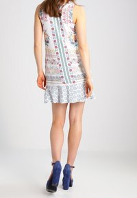 Sansihame, jolla on kukkakuosi ja geometrinen kuvio valkoisina, sinisinä ja vihreinä sävyinä, flare-alareuna ja teksturoitu kangas.