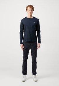 Langærmet navyblå skjorte med rund hals, parret med mørke bukser og hvide sneakers. Enkel design, glat tekstur og ingen synlige mønstre.