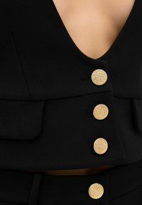 Svart väst med djup V-hals, tre utsmyckade guldknappar och två sidofickor, tillverkad av ett slätt, texturerat tyg.