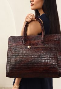 Brown crocodile-embossed leather tote bag with dual handles, front zip pocket, and gold hardware accents. Textured surface with a glossy finish.