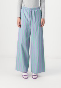 Wide-leg pants in lavender with green vertical stripes. Elastic waistband and smooth fabric. Worn with white socks and purple sandals.