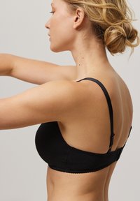 Sujetador negro con un acabado de tela suave. Presenta tirantes ajustables, un cierre de gancho y ojal, y un delicado borde ondulado a lo largo de los bordes.
