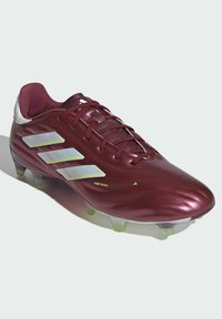 Scarpa da calcio color marsala con finitura lucida, dotata di tre strisce riflettenti argento, lacci piatti e tacchetti di colore verde per la presa.