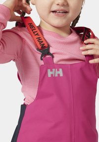 Růžový snowsuit se šedým logem, nastavitelné červené popruhy s černým textem. Měkká textura, navrženo pro teplo a venkovní aktivity.