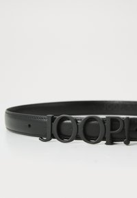 Black leather belt featuring a glossy black logo buckle that reads "JOOP!". The belt has a smooth texture and minimalist design.