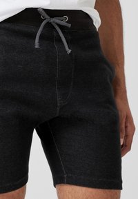 Shorts de sport noirs en mélange de coton avec une texture lisse. Ils présentent une ceinture élastique avec un cordon de serrage et des surpiqûres contrastantes.