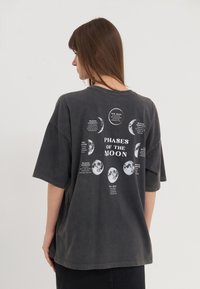 Dark gray oversized t-shirt featuring a moon phases graphic on the back with text descriptions surrounding each phase. Short sleeves, soft texture.