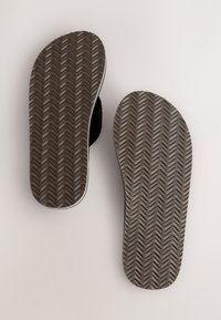 Semelles de sandales noires avec un motif texturé ondulé, présentant un bord lisse et une bordure blanche contrastante.