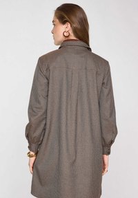 Vestito camicia a maniche lunghe marrone a quadri con colletto, dettaglio arricciato sul retro e polsini con bottoni. Tessuto dalla texture liscia.