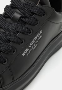 Sneaker in pelle nera con lacci neri testurizzati, superficie liscia e logo bianco in rilievo sul lato. Punta arrotondata e suola ammortizzata.