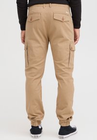 Khaki cargo bukser med elastiske manchetter, flere lommer og knapdetaljer. Lavet af slidstærkt stof, med en afslappet pasform og tapered ben.