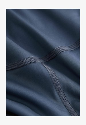 Marineblauer Stoff mit glatter, matter Oberfläche. Mit kontrastierenden Nähten im Karomuster, die die weiche Textur des Materials betonen.