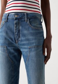 Blue denim jeans featuring a mid-rise waist, five pockets, and contrast stitching. Smooth texture with a classic fit design.
