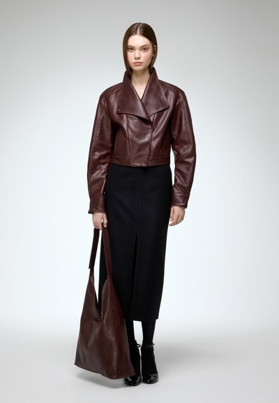 Burgundy leather cropped jacket with large collar, paired with a fitted black skirt. Model holds a matching leather tote bag.