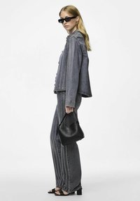 Giubbotto di denim e pantaloni grigi scuri con cuciture bianche a contrasto. Gli accessori includono occhiali da sole neri e una borsa, completati da sandali neri.