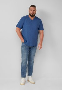 Niebieska krótka koszulka z dekoltem w serek, połączona z jasnymi dżinsami i białymi trampkami. Gładka faktura, luźny krój i minimalistyczny design.