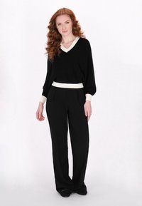 Pulover negru cu decolteu în V alb și manșete albe, asortat cu pantaloni negri cu talie înaltă. Are o croială lejeră și o textură moale.
