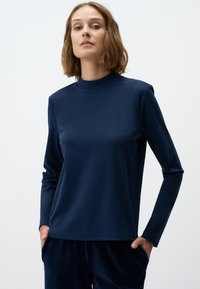 Navyblauwe langemouwen top met hoge hals, gemaakt van zachte stof. Heeft een relaxte pasvorm en een gladde textuur, gecombineerd met donkere broeken.