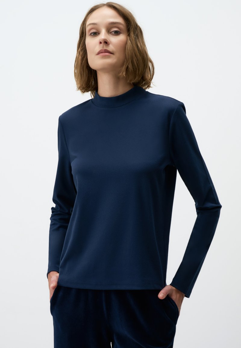 Navyblauwe langemouwen top met hoge hals, gemaakt van zachte stof. Heeft een relaxte pasvorm en een gladde textuur, gecombineerd met donkere broeken.