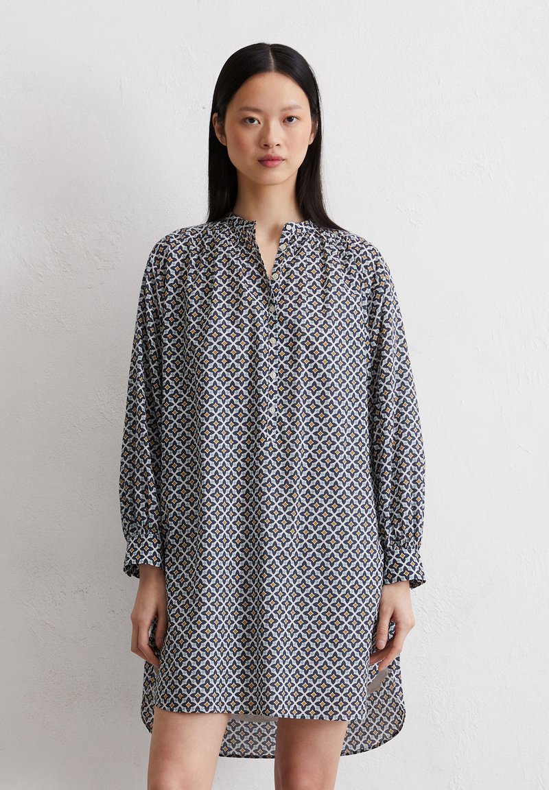 Langärmliges Tunika-Kleid in navy, weiß und gelb mit geometrischem Muster; verfügt über einen Stehkragen und leichte Raffung an den Schultern.