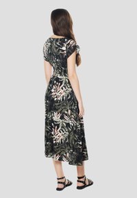 Robe midi à motif floral en vert foncé avec des accents roses, dotée de manches courtes et d'une taille cintrée. Portée avec des sandales noires à brides.