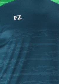 Mörkblå sporttröja med ett subtilt vågmönster, har en grön halsringning och vitt "FZ"-logotyp på framsidan. Slät tygtextur.