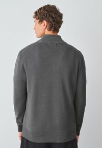 Grijze gebreide trui met een hoge kraag, geribde manchetten en zoom. De stof lijkt zacht met een gladde textuur en een gestructureerde pasvorm.
