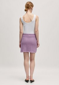 Witte mouwloze top met brede ronde rug, gecombineerd met een lila gehaakte mini-jurk met een diamanten patroon. Soepele textuur, aansluitend ontwerp.