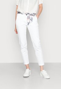 White cotton pants with a floral-patterned belt, featuring a tailored fit and cuffed ankles, paired with white sneakers.