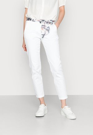 Pantalons en coton blancs avec une ceinture à motif floral, dotés d'une coupe ajustée et de chevilles retroussées, associés à des baskets blanches.