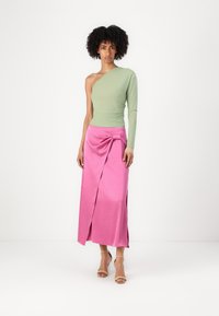 Green one-shoulder top paired with a pink wrap skirt featuring a front knot detail. Smooth textures and contrasting colors emphasize the design.