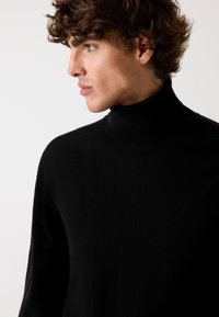 Maglione a collo alto nero realizzato in un tessuto morbido, con un design aderente e polsini a costine. Stile minimalista senza motivi visibili o hardware.