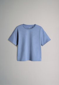 T-shirt bleu clair à manches courtes et col rond suspendu sur un fond gris clair uni.