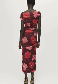 Robe cintrée avec un décolleté bardot, présentant un motif floral rouge et rose sur fond bordeaux ; longueur genou avec texture froncée.